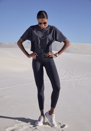 Cropped grey t-shirt with short sleeves, ribbed black leggings, and light-colored sneakers. Smooth fabric and athletic fit.