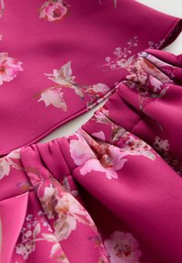 Tkanina o kwiatowym wzorze w żywym różowym odcieniu, charakteryzująca się miękką fakturą i marszczeniem przy szwie, przedstawiająca delikatne motywy kwiatowe.