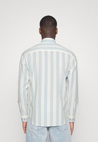 Camicia a maniche lunghe a righe azzurro chiaro e bianco, con polsini bottonati, colletto classico, tessuto morbido, orlo curvo e dettagli di cucitura a vista.