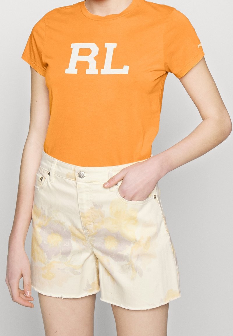 Orange bomullströja med vit "RL"-logotyp, ihopparad med krämfärgade shorts med ett blommönster i gult och ljuslila.