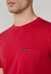 Rode katoenen T-shirt met een ronde halslijn, voorzien van een borstzak met een blauw label. Zachte textuur en korte mouwen.