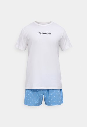 T-shirt en coton blanc avec logo "Calvin Klein" noir, associé à un short bleu orné de petits logos CK blancs. Design décontracté.
