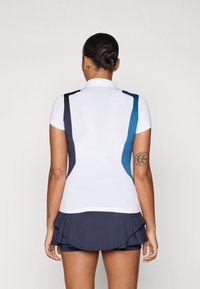 White polo shirt with short sleeves, featuring navy and teal accents on the sides. Paired with a navy pleated skirt.