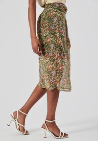 Jupe midi imprimée florale dans des teintes de vert, orange, rose et violet avec un tissu léger et fluide. Associée à des talons blancs à lanières.