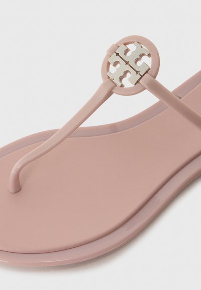 Tongs en caoutchouc roses avec un accent métallique rond et un design de logo en quatre parties. Texture lisse et design minimaliste avec des bords arrondis.