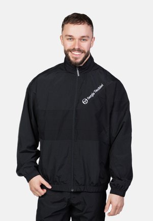 Schwarze Windjacke mit vollem Reißverschluss, langen Ärmeln, elastischen Bündchen und Logo auf der linken Brust. Leichtes Material mit glatter Textur.