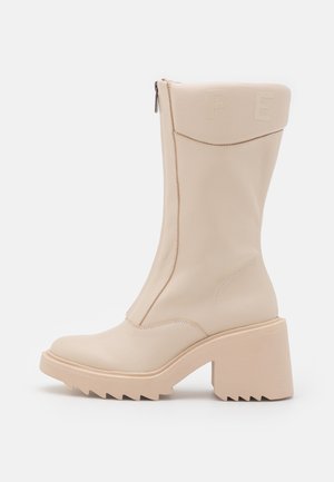 Beige læderstøvle til midt på læggen med chunky hæl, robust sål, sidelukning med lynlås og præget "P E" bogstaver nær toppen.