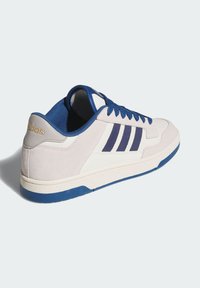 Bijela i svijetlosiva atletska tenisica s plavim vezicama, plavim naglascima i tri tamnoplave pruge sa strane. Gumeni potplat s teksturiranom površinom.