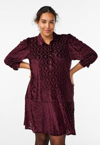 Bordowa aksamitna sukienka z kołnierzykiem zapinanym na guziki, teksturowanym kwiatowym wzorem, długimi bufiastymi rękawami i rozkloszowanym dołem, z bocznymi kieszeniami.