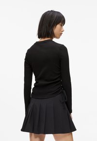 Czarny prążkowany top z długim rękawem o marszczonych bokach, zestawiony z czarną plisowaną spódnicą. Tkanina jest gładka i dobrze dopasowana.