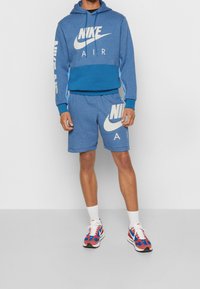 Blå Nike sweatshirt med vitt logo, tillsammans med matchande shorts med logo. Vita sneakers med röda och blå accenter.