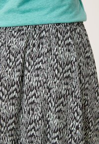 Jupe noire avec un motif abstrait blanc et bleu clair, taille élastique et tissu léger. Portée avec un haut vert menthe.