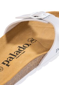Infradito bianche con una larga fascia e fibbia, poggiapiedi in sughero e rivestimento in suede beige. Presenta il logo impresso "palado" e "Made in Spain."