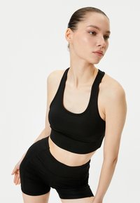 Sort atletisk crop top og matchende shorts, lavet af glat stof. Toppen har en rund halsudskæring og brede stropper; shortsene har en tætsiddende design.