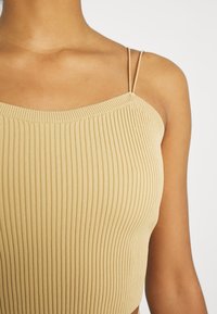 Top court côtelé beige avec des fines bretelles ajustables et un décolleté carré, au design ajusté et à la texture douce.