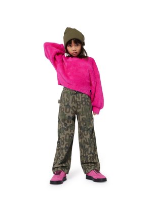 Fluffy roze sweater, olijfgroene broek met grote zwarte letters en roze sneakers met zwarte zolen, gedragen met een bijpassende olijfkleurige beanie.