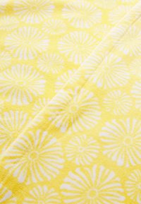 Tessuto giallo con una superficie texture caratterizzata da un motivo floreale bianco ripetuto. Attenzione al materiale morbido e assorbente.