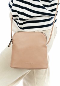 Skórzana listonoszka w kolorze brązowym o gładkiej fakturze, zaokrąglonym dnie i zapięciu na zamek błyskawiczny. Posiada wytłoczone logo z przodu. Regulowany pasek.