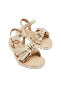 Sandali metallici dorati con dettaglio a nodo sulla parte anteriore, caratterizzati da un motivo a pois su una soletta beige e una suola bianca.