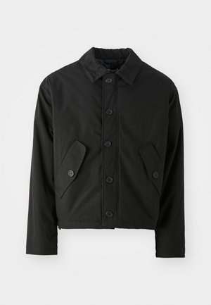 Veste noire courte en tissu lisse. Présente un devant à boutons, un col pointu et deux poches angulaires sur les côtés.