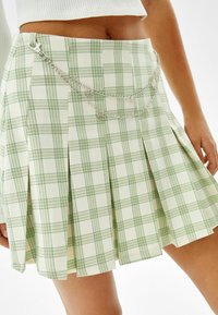 Grön och krämrutigt kjol med veck och en silverkedjedetalj runt midjan, med fina linjer och en smidig textur.