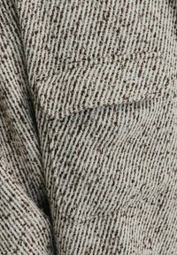 Gros plan sur un tissu en laine chevrons marron et crème avec un détail de poche à rabat sur un vêtement.