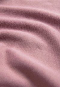Textilná látka v jemnej ružovej farbe, hladká textúra, mierne natiahnutá a preložená, predvádzajúca rovnomerné tkanie a jemný lesk.