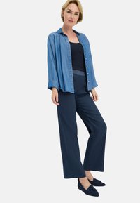 Hellblaues Denim-Hemd mit Knöpfen, schwarzes Tanktop, marinefarbene weite Hose und schwarze Ballerinas mit Quasten. Glatte Texturen und lässige Passform.