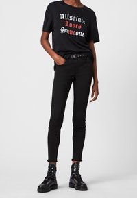 Černé bavlněné tričko s červeným a bílým textem "Allsaints Loves Someone" spárované se slim-fit černými džíny a černými šněrovacími bojovými botami.
