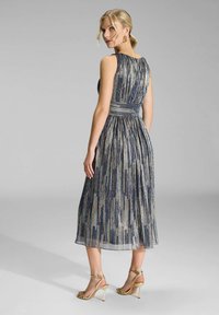 Une robe sans manches de mi-longueur présente des plis verticaux en bleu métallique et argent. La robe a une taille ajustée et une jupe évasée, accompagnée de talons dorés.
