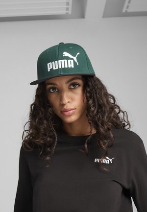 Zelena snapback kapa s bijelim "PUMA" logom i grafikom mačke; ravni vizir; nošena s crnom majicom koja ima mali logo na prsima.