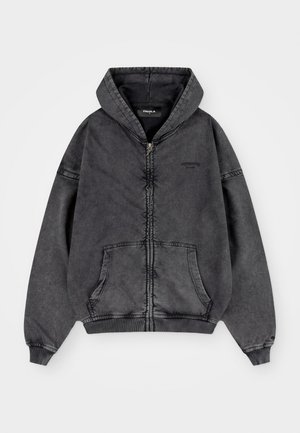 Pilkas džemperis su gaubtu, užtrauktuku priekyje, dviem priekinių kišenių ir ribomis rankogaliuose. Išsiskiria išblukusia tekstūra ir minimalia krūtinės zona ženklinimu.