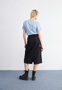 Light blue short-sleeve t-shirt paired with a black, knee-length skirt featuring an elastic waist and large pockets. Black lace-up boots complete the look.