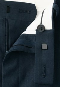 Tmavomodrý pás na nohaviciach so zipsom, gombíkom a kovovou háčikovou sponou, odhaľujúci bielu látkovú podšívku vnútri.