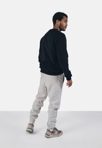 Sweatshirt noir, joggeurs gris, et baskets beige. Le sweatshirt a un col rond, les joggeurs ont des poignets élastiques, et les baskets présentent une marque bien visible.