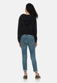 Sudadera negra recortada con capucha, combinada con jeans de mezclilla azul claro, con una silueta ajustada y puños enrollados. Zapatillas con estampado de leopardo.