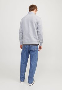 Sudadera gris con cuello alto y dobladillo acanalado, combinada con unos vaqueros de denim azul sueltos. La tela parece suave y texturizada.