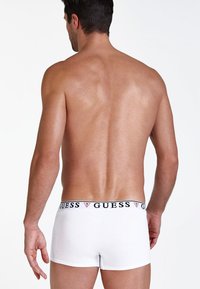 Fehér pamut boxer alsónemű, fekete derékszárral, rajta a "GUESS" logóval. Simaság jellemzi, testhezálló fazonnal, hátulról látható.