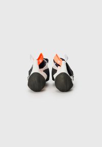 Sapatos de escalada com um design em preto e branco, apresentando um destaque traseiro em laranja, solas de borracha e um acabamento texturizado para maior aderência.