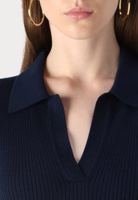 Top a coste blu navy con scollatura a collo e apertura a V. Caratterizzato da una superficie testurizzata e cuciture visibili lungo i bordi del collo.