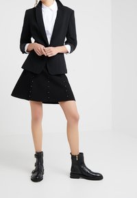 Blazer nero con colletto a scialle, abbinato a una gonna nera con borchie argentate. Stivaletti neri alla caviglia con zip laterale e dettagli con cinturini.
