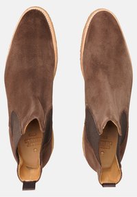 Hnědé semišové kotníkové boty s elastickými bočními panely, kulatými špičkami a kontrastními světle hnědými gumovými podrážkami. Bez viditelných vzorů nebo kovových doplňků.