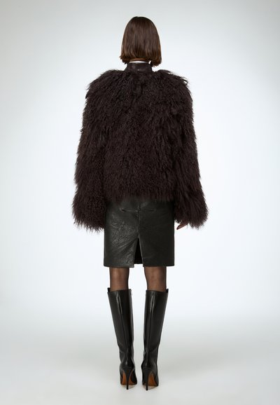 Puszysta czarna futrzana kurtka z szerokimi rękawami, zestawiona z dopasowaną czarną skórzaną spódnicą i wysokimi czarnymi botkami na szpilce do kolan.