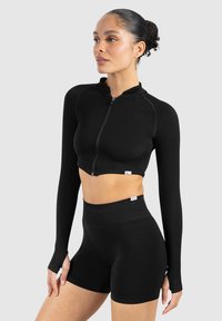 Sort cropped zip-up jakke med lange ærmer og matchende høj taljede shorts. Fremstillet af strækbart stof med en glat tekstur.