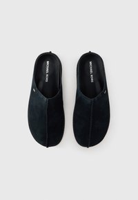 Suede slip-on shoes in dark navy color with a smooth texture, featuring a stitched seam down the center and a branded insole.