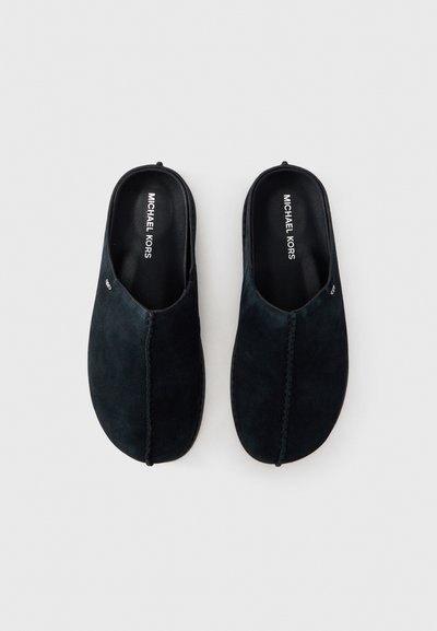 Chaussures sans lacets en daim de couleur bleu marine foncé avec une texture lisse, présentant une couture centrée et une semelle intérieure de marque.