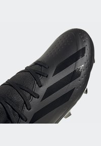Scarpa da calcio nera con tomaia testurizzata, design elegante con tre evidenti strisce e lacci neri su una finitura opaca.