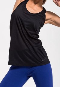 Czarna sportowa koszulka bez rękawów o luźnym kroju i szerokim dekolcie, zestawiona z dopasowanymi niebieskimi legginsami, z małym logo Nike na koszulce.
