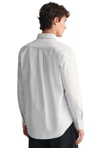 Camicetta a righe bianche e blu con maniche lunghe, polsini con bottone e colletto classico. Il retro presenta un pezzo di yoke e pieghe per una maggiore libertà di movimento.