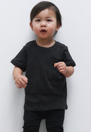 Sort kortærmet t-shirt med rund halsudskæring og to trykknapper på skuldrene, parret med sorte bukser. Glat bomuldsstof, afslappet pasform.